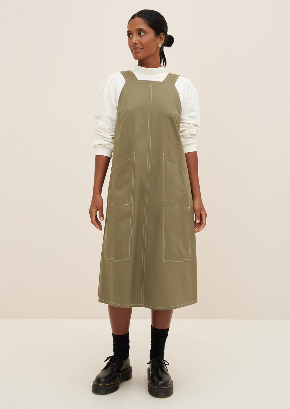 A woman wearing a pinafore style dress in khaki color.