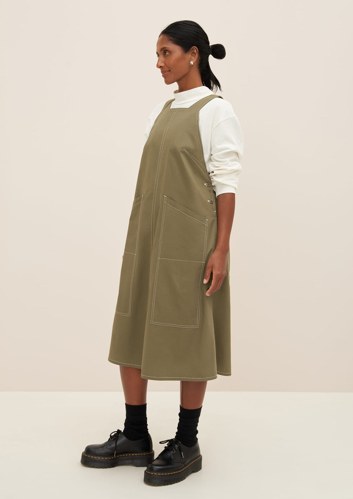 A woman wearing a pinafore style dress in khaki color.