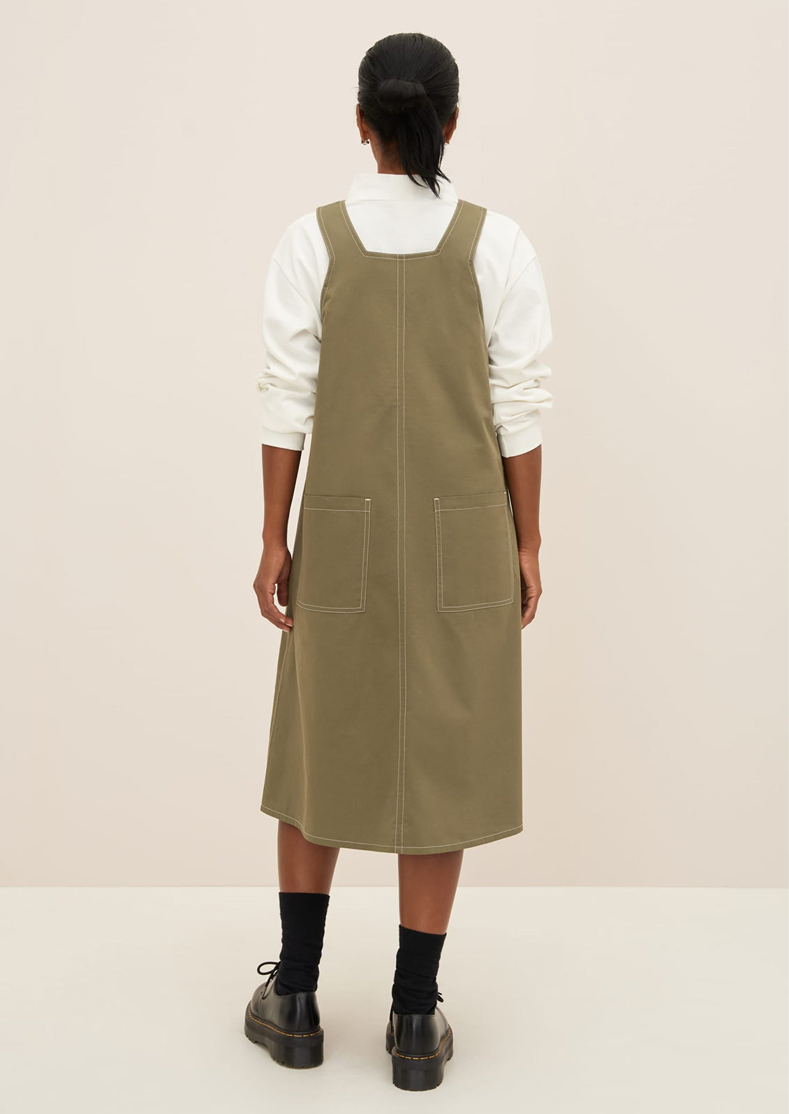 A woman wearing a pinafore style dress in khaki color.