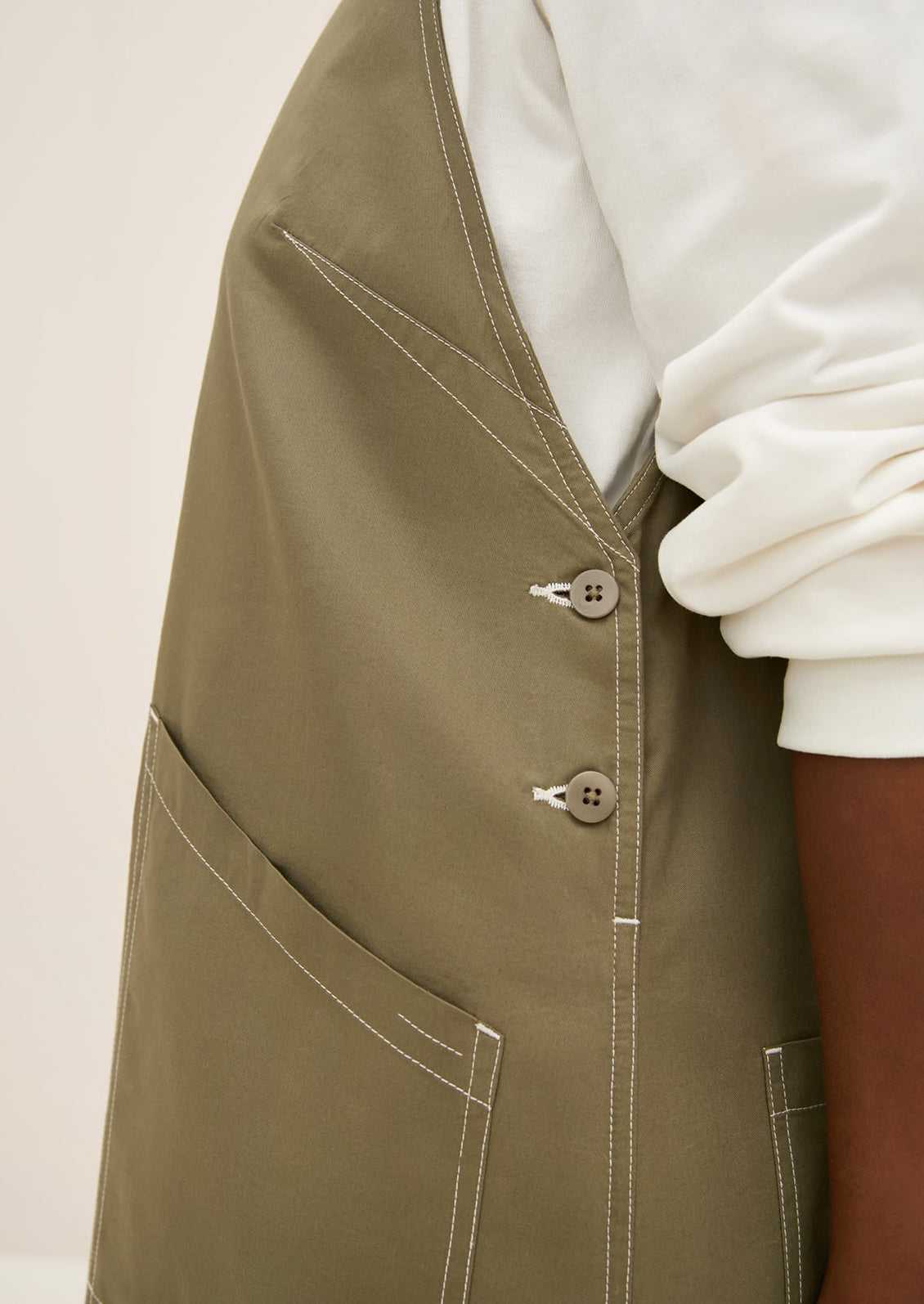 A woman wearing a pinafore style dress in khaki color.