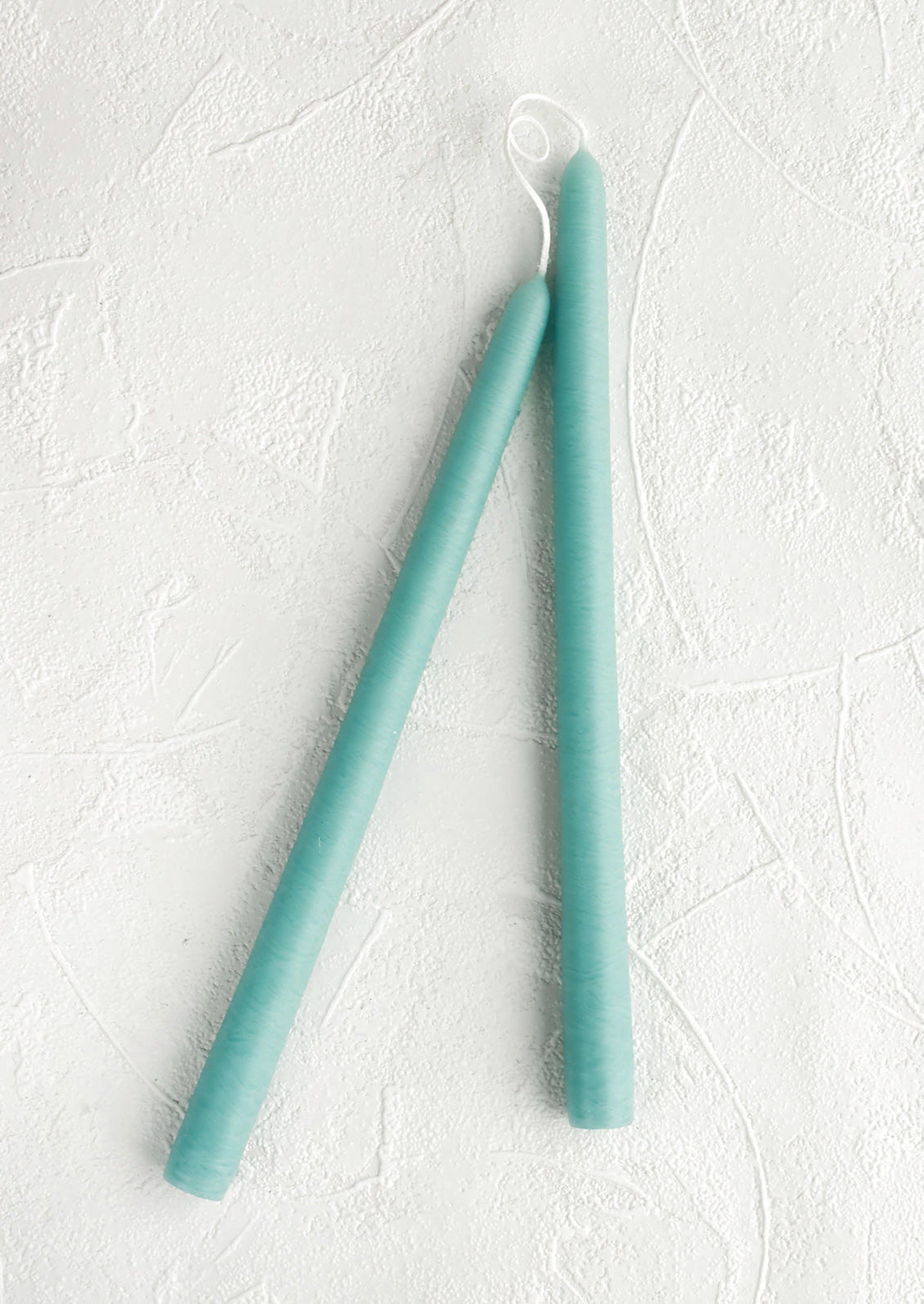 Two teal candles on a textured white surface