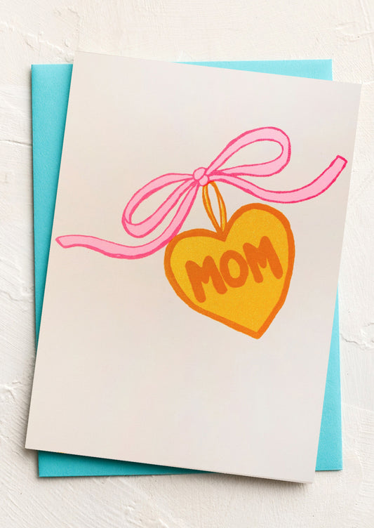 Greeting card with a heart-shaped candy and 'MOM' text on a white background