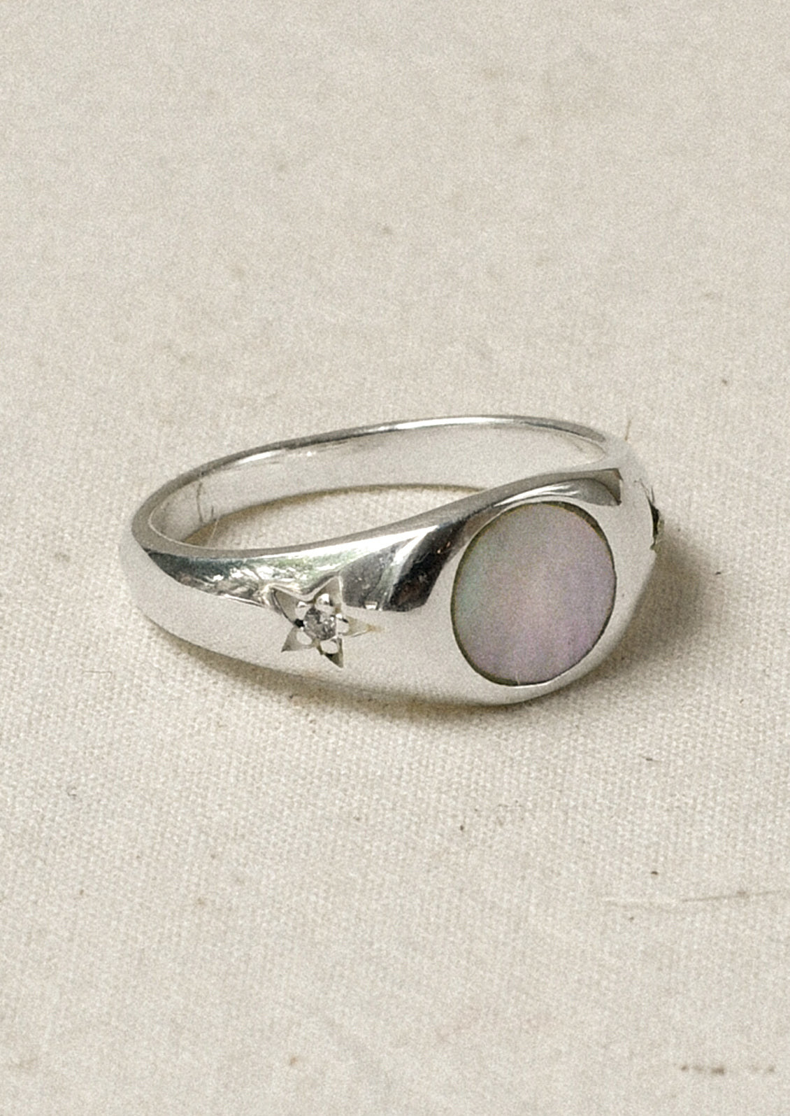 A sterling silver ring with a mother of pearl center and carved out stars on either side with a flower in the middle.