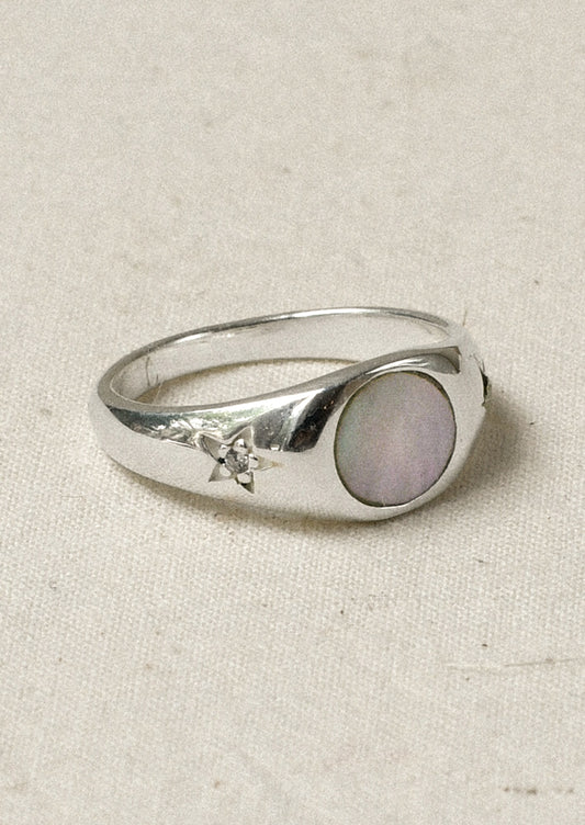 A sterling silver ring with a mother of pearl center and carved out stars on either side with a flower in the middle.