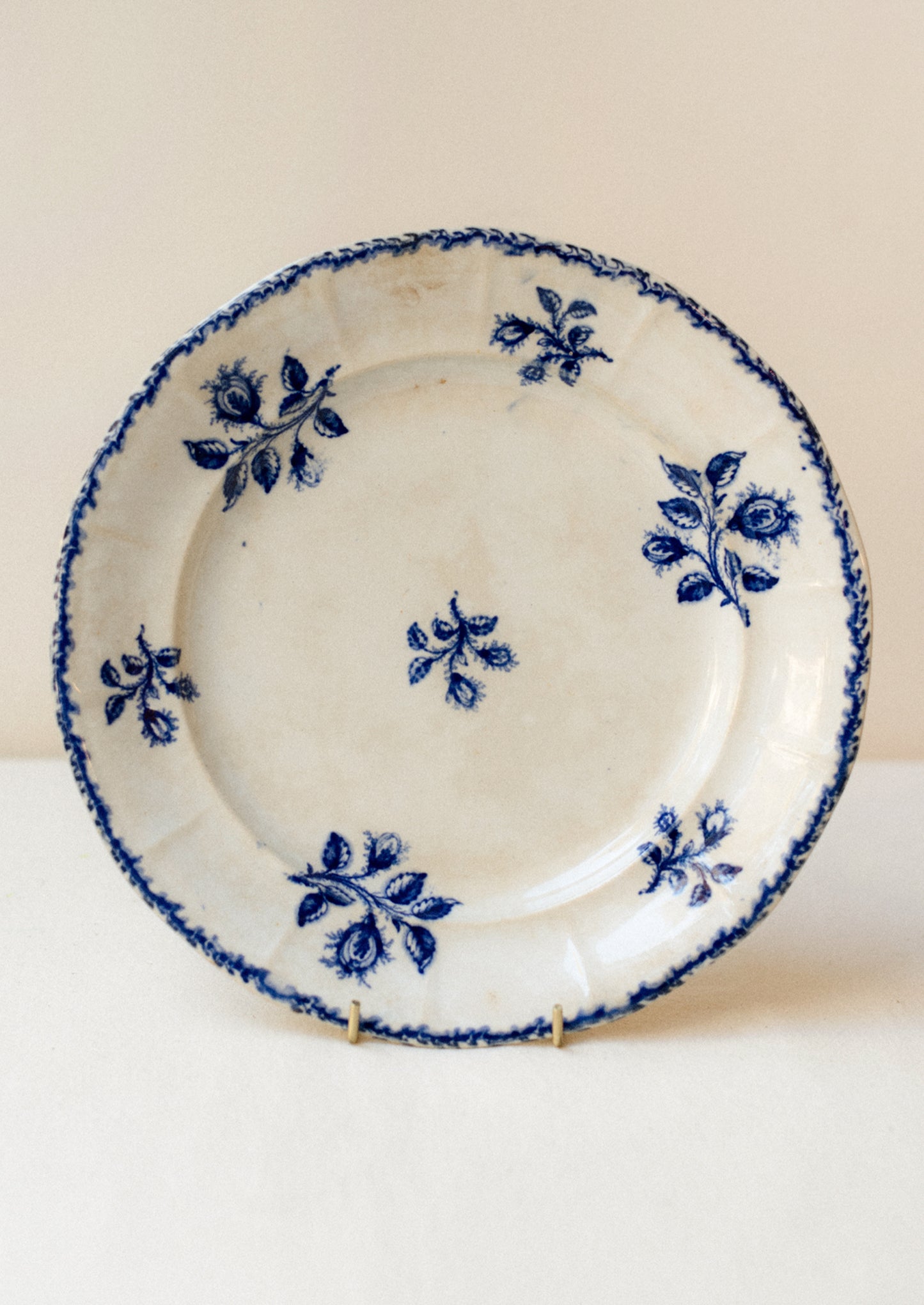 An antique ceramic plate in ivory with blue floral pattern and stamped rim.