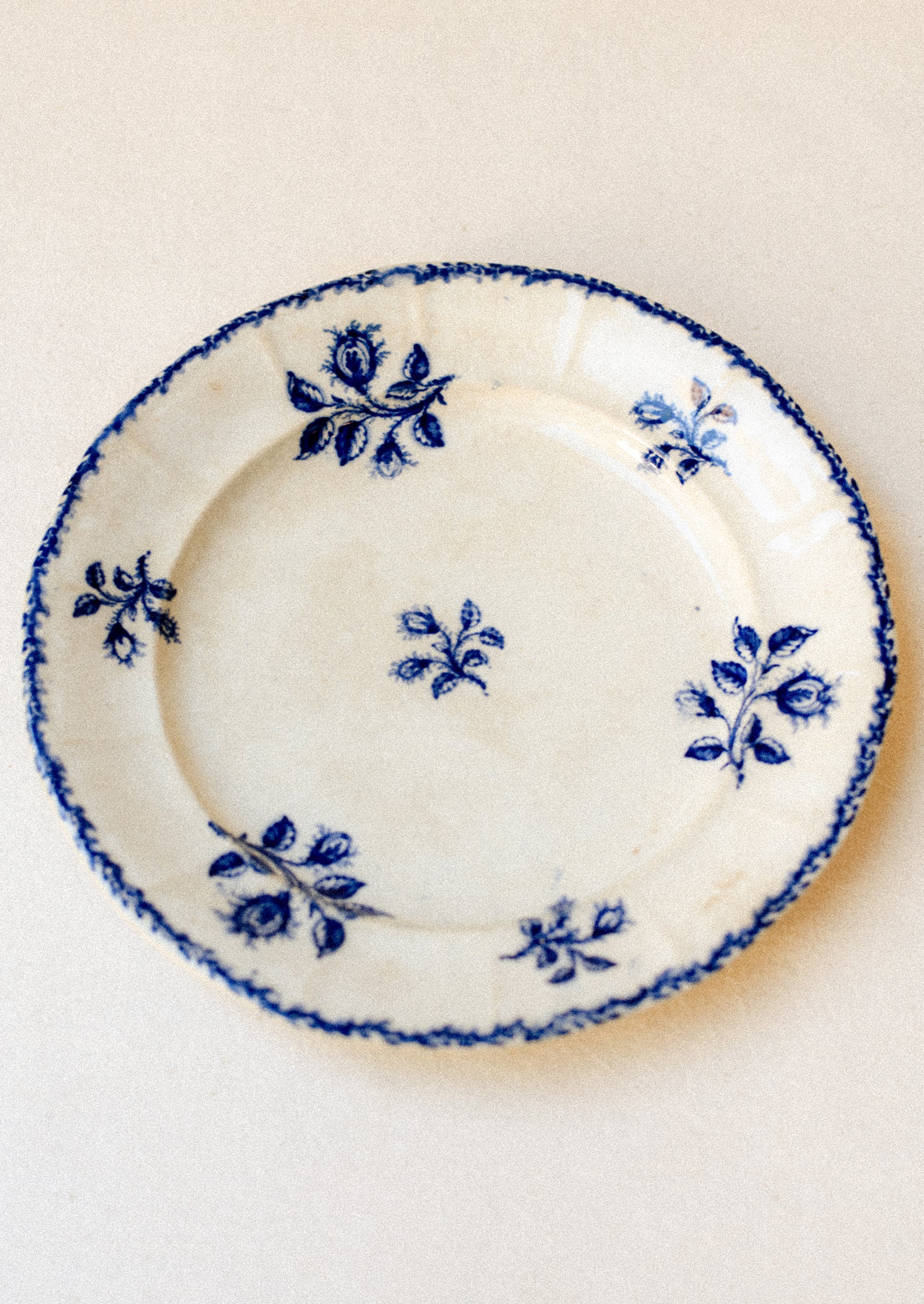 An antique ceramic plate in ivory with blue floral pattern and stamped rim.