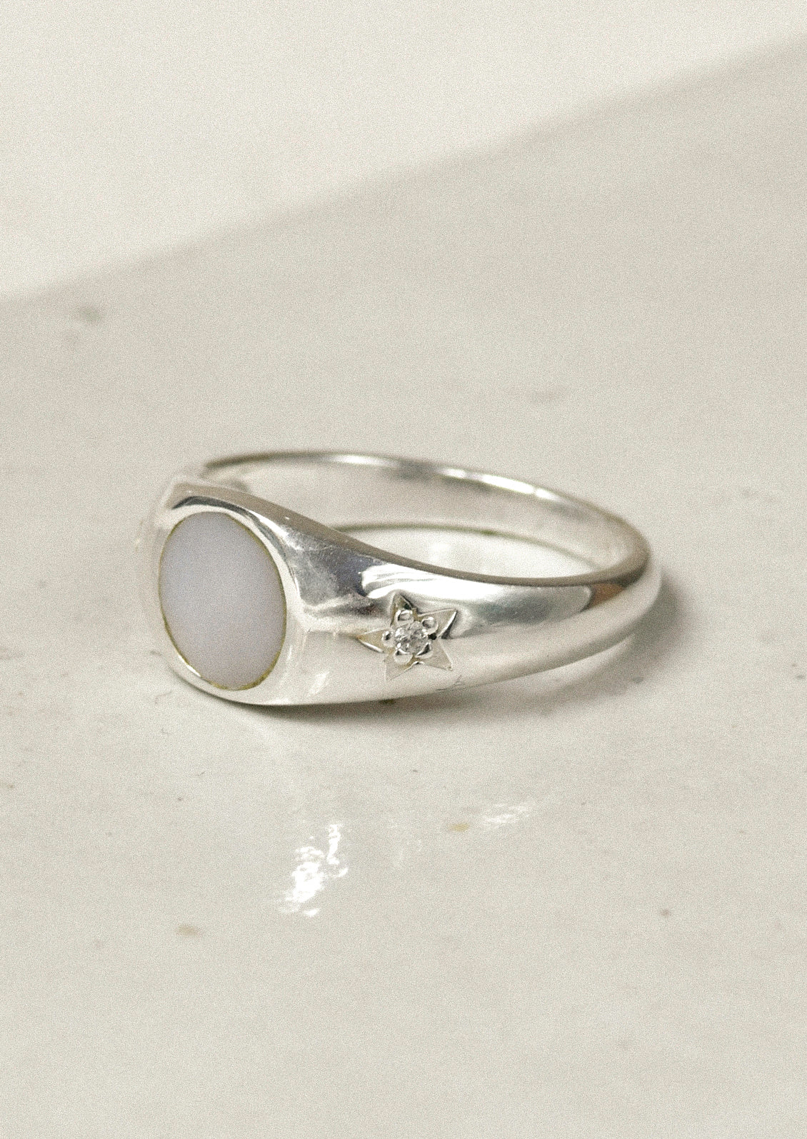 A sterling silver ring with a mother of pearl center and carved out stars on either side with a flower in the middle.