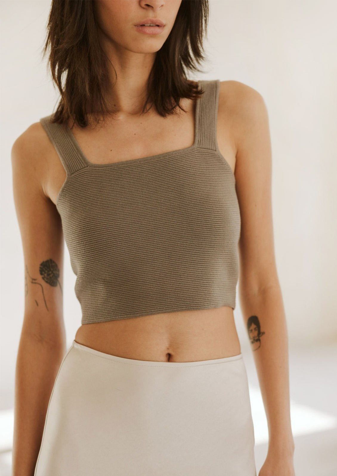 A woman wearing a form fitting square neck tank top in greige color.
