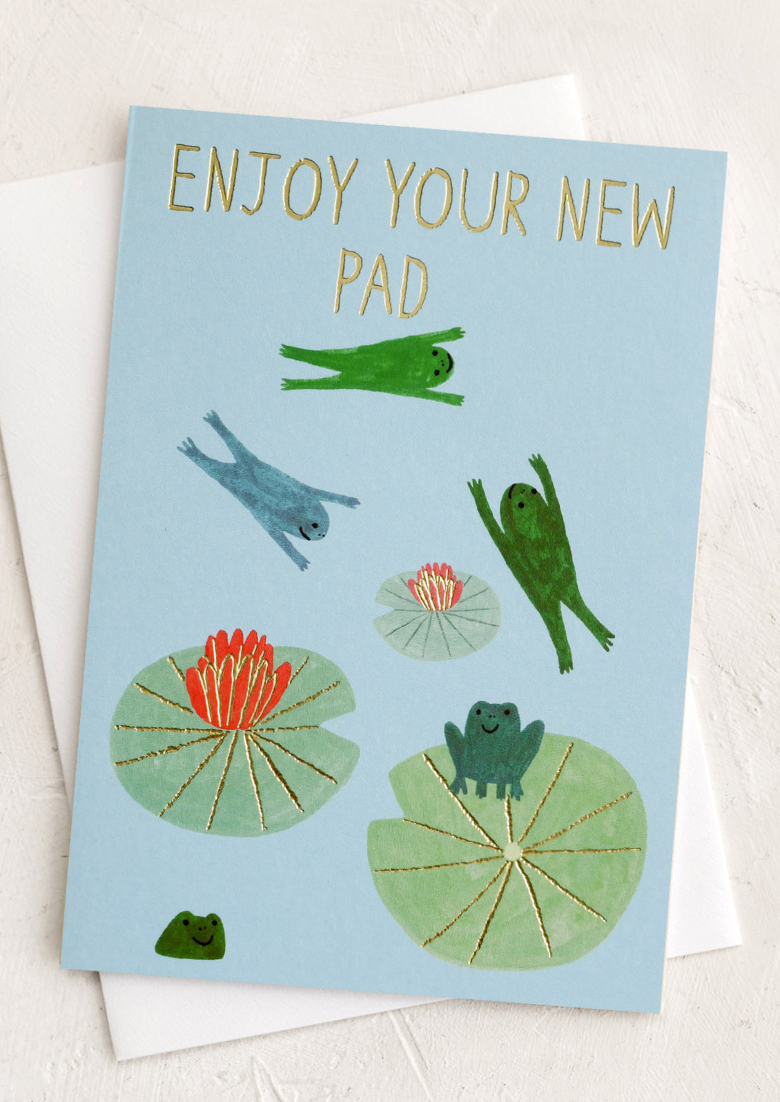 A greeting card with illustration of frogs on lily pads, text reads "Enjoy your new pad".