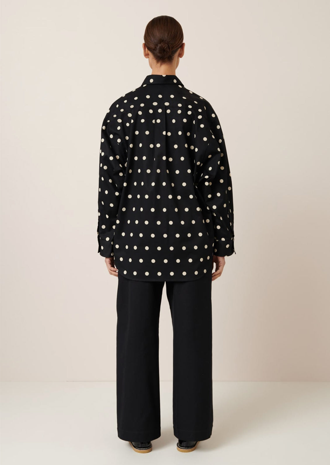 A woman wearing an oversized button front shirt in black with white polka dots.