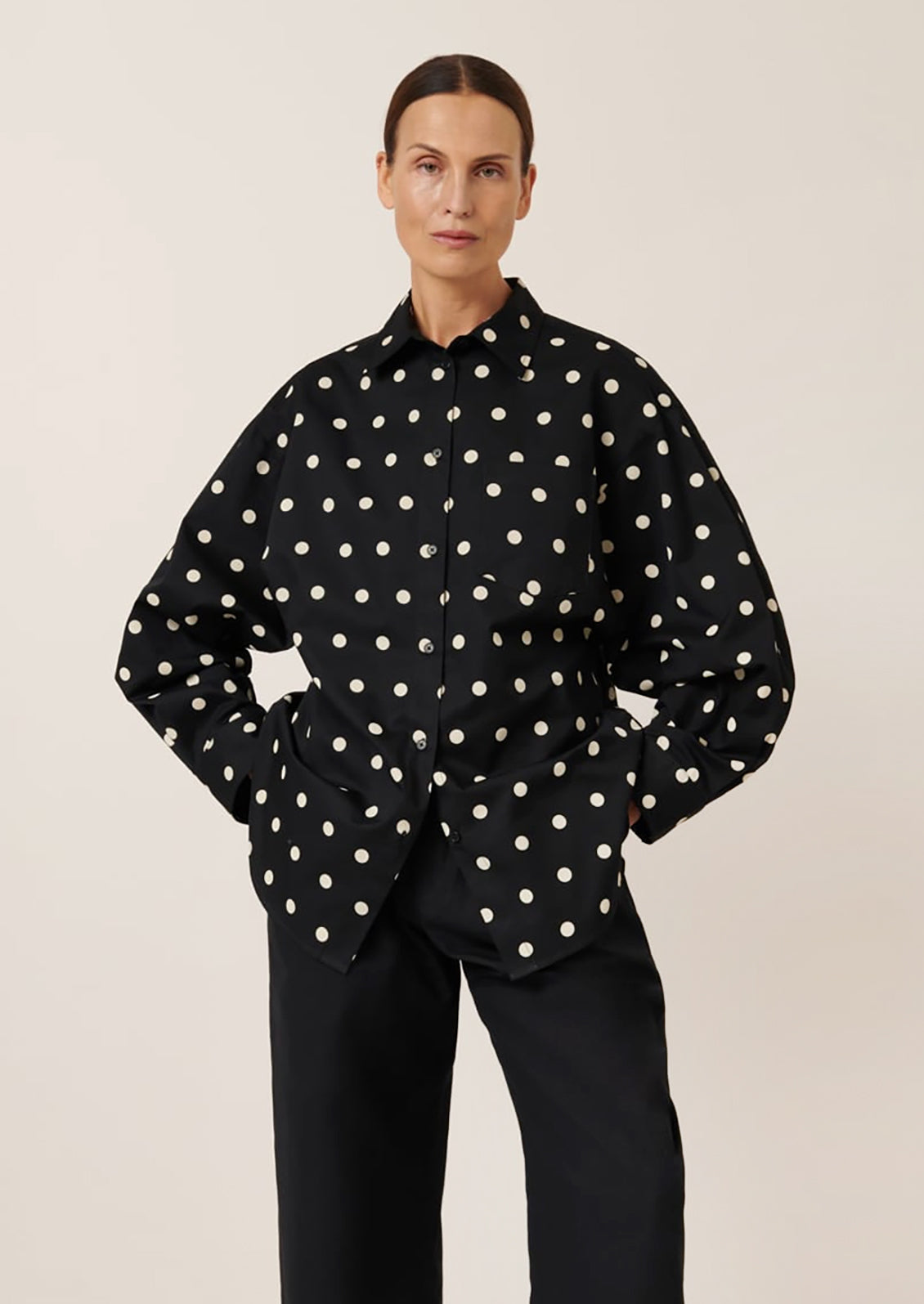 A woman wearing an oversized button front shirt in black with white polka dots.