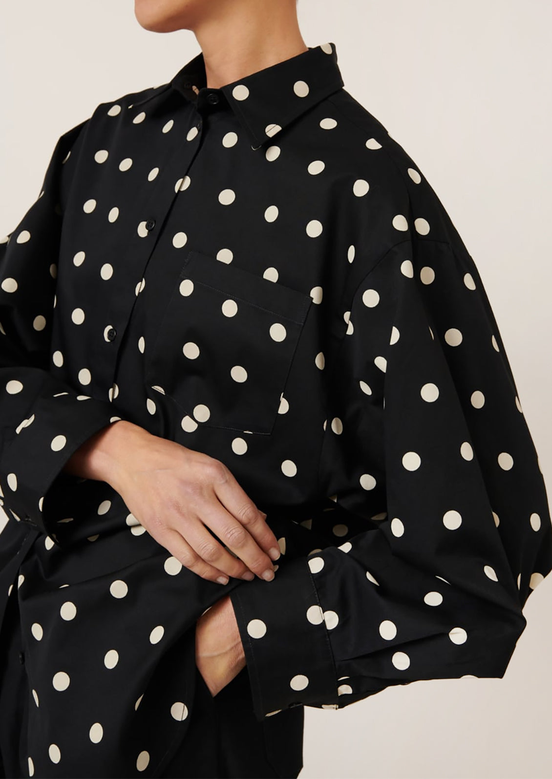 A woman wearing an oversized button front shirt in black with white polka dots.