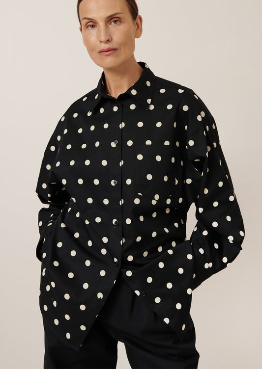A woman wearing an oversized button front shirt in black with white polka dots.