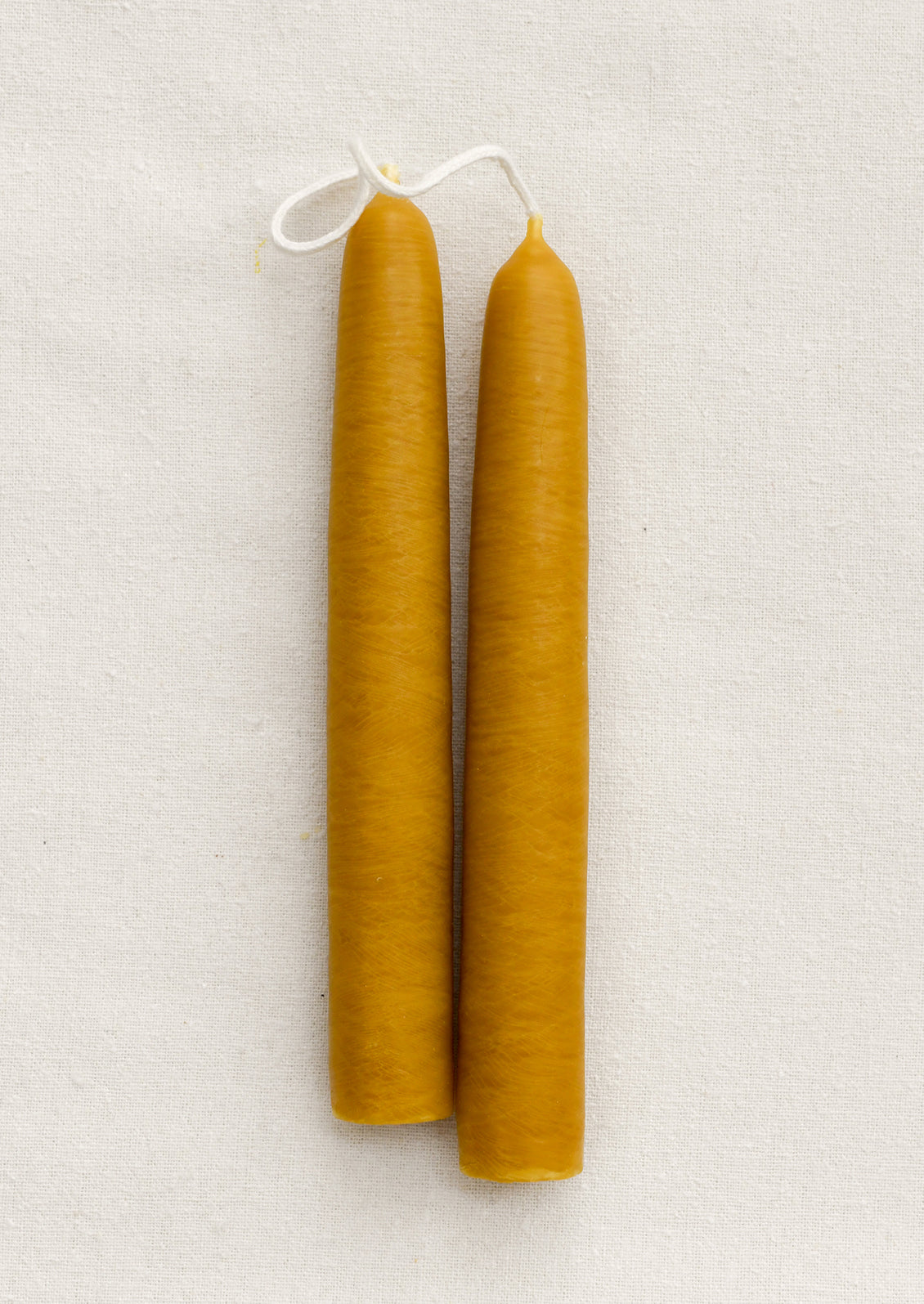 A pair of short ochre taper candles on a brown background.