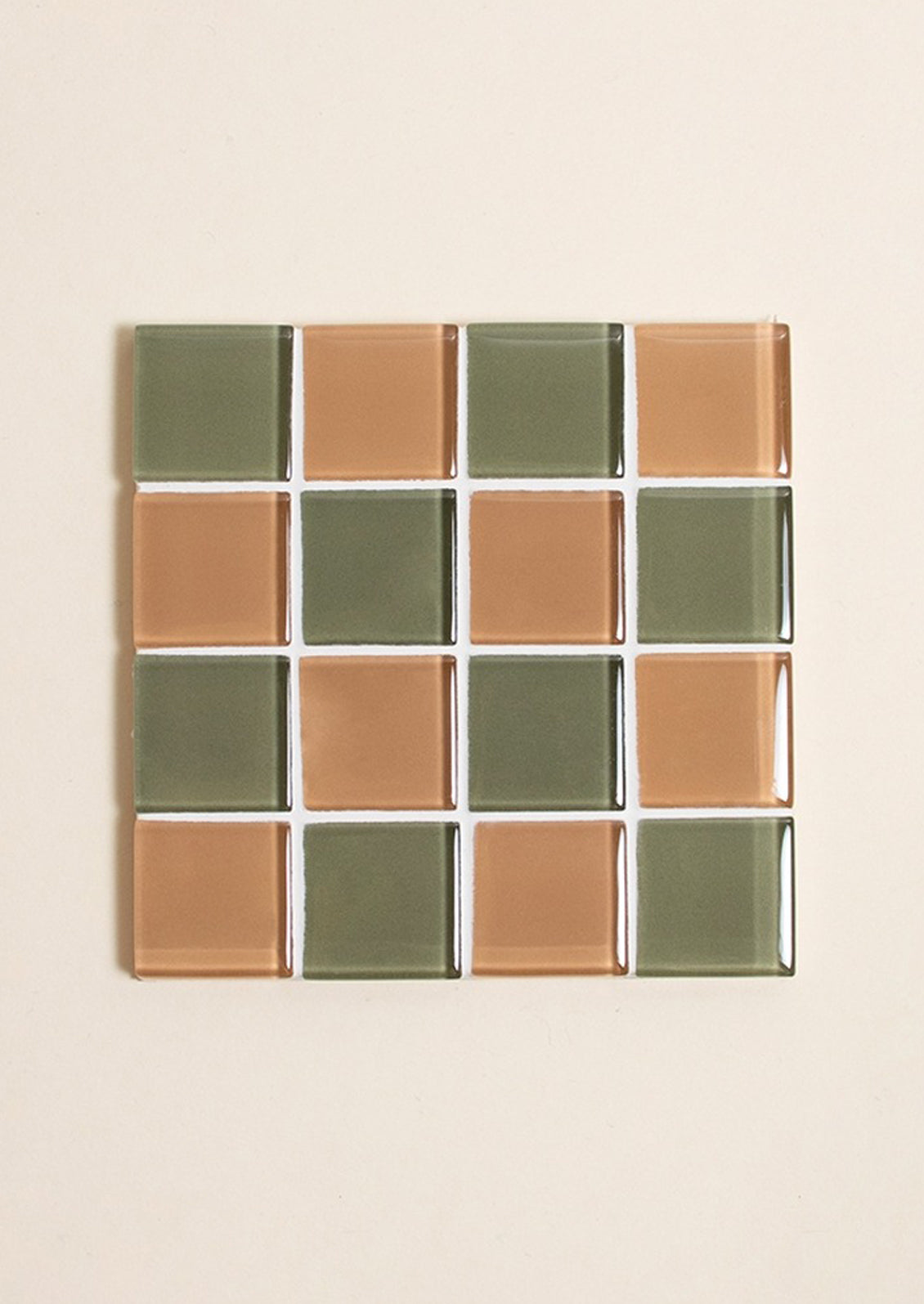 A glass tile coaster in two tone checker pattern in olive green and chocolate brown.