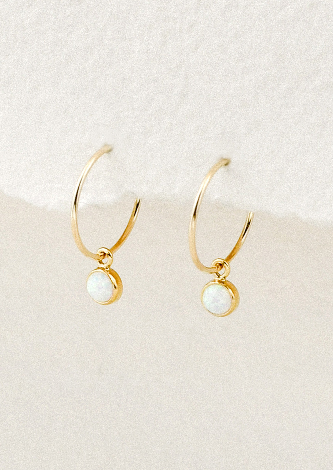 A pair of small gold hoop earrings with bezeled opal charms.