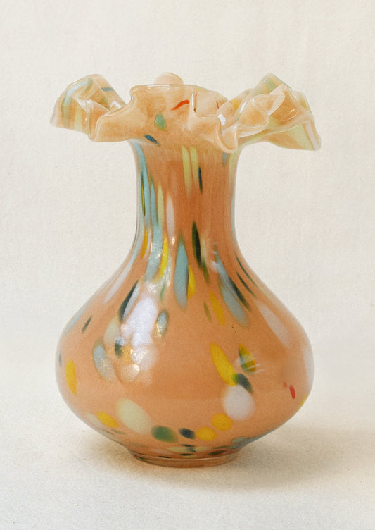 A handblown glass vase with a peach colored body, multicolor paint strokes, and a ruffled opening.
