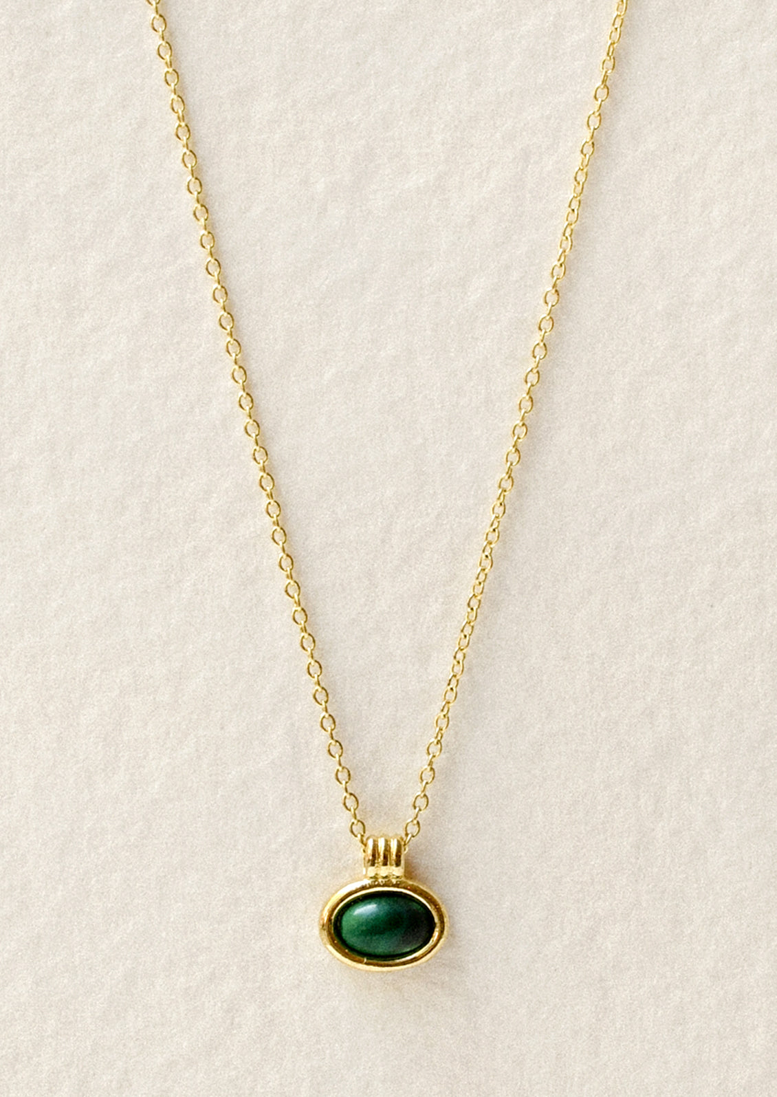 A gold necklace with an oval green gemstone charm.