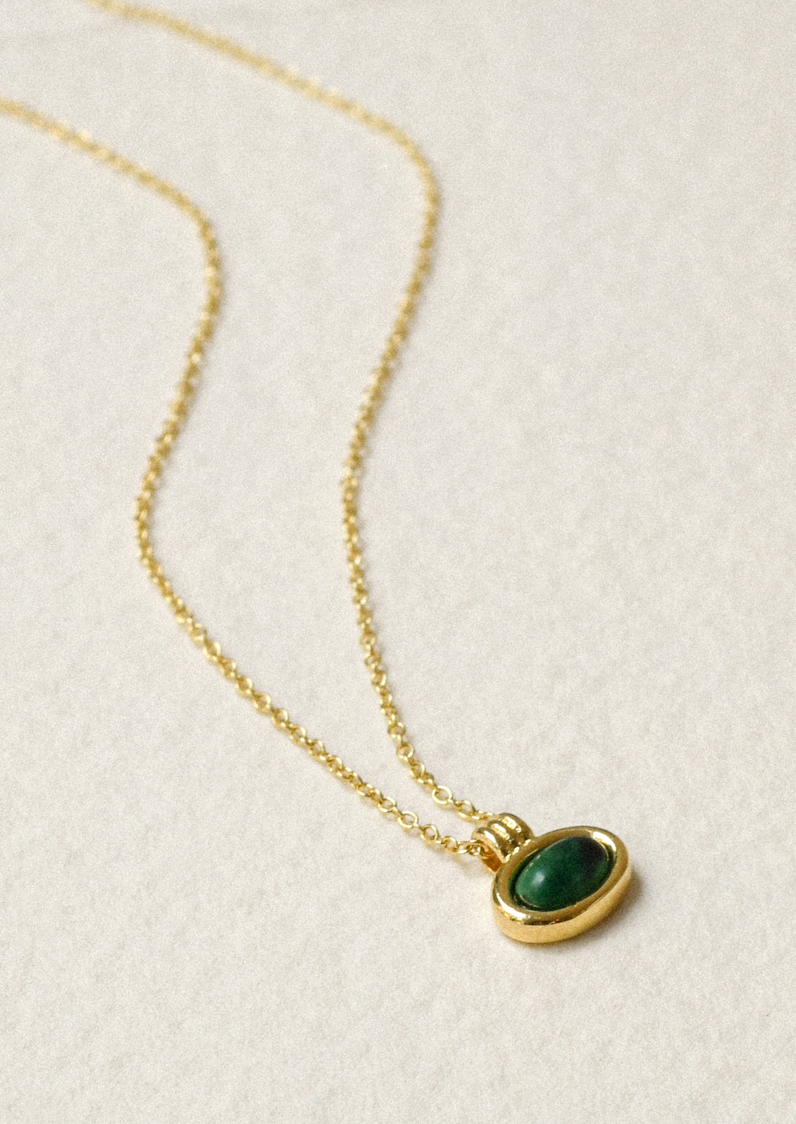 A gold necklace with an oval green gemstone charm.