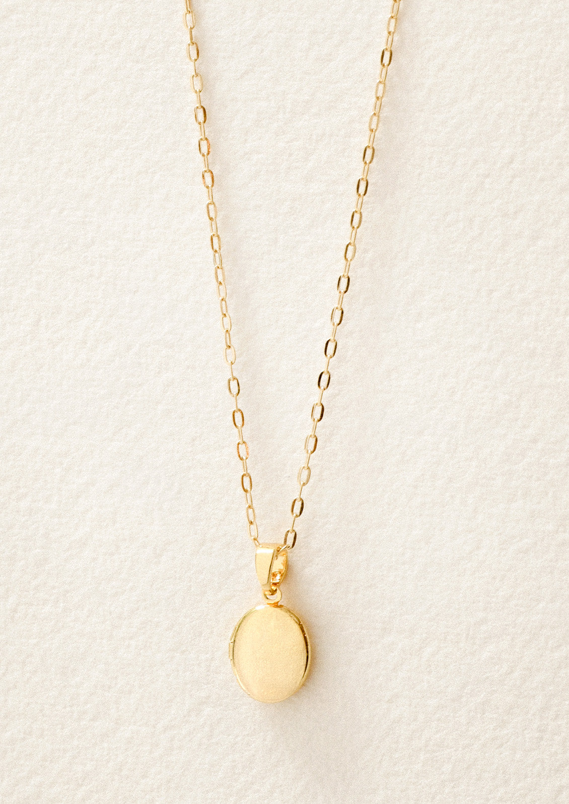 A gold chain necklace with a small oval locket pendant on a white background.