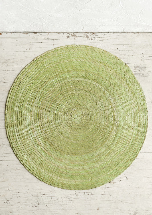 A round woven straw placemat in pistachio color.