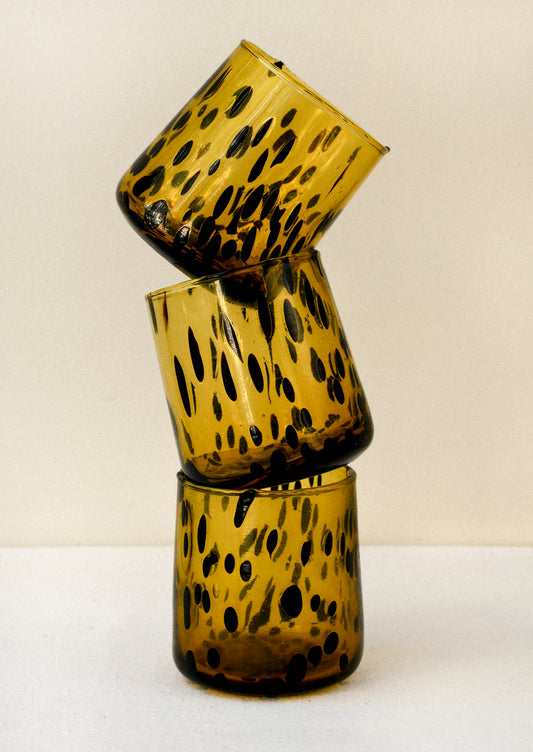 A stack of dark yellow drinking glasses with black abstract spots.