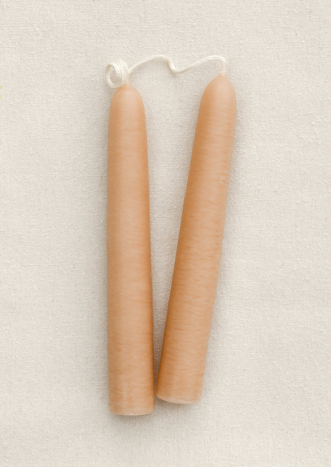 A pair of short nude taper candles on a brown background.