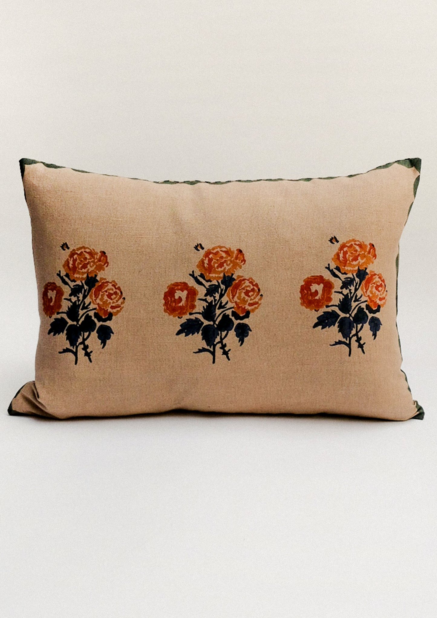 Beige pillow with rust colored floral print and scalloped green border.