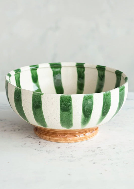 A large ceramic bowl in white with painted vertical green stripes and brown footed base.