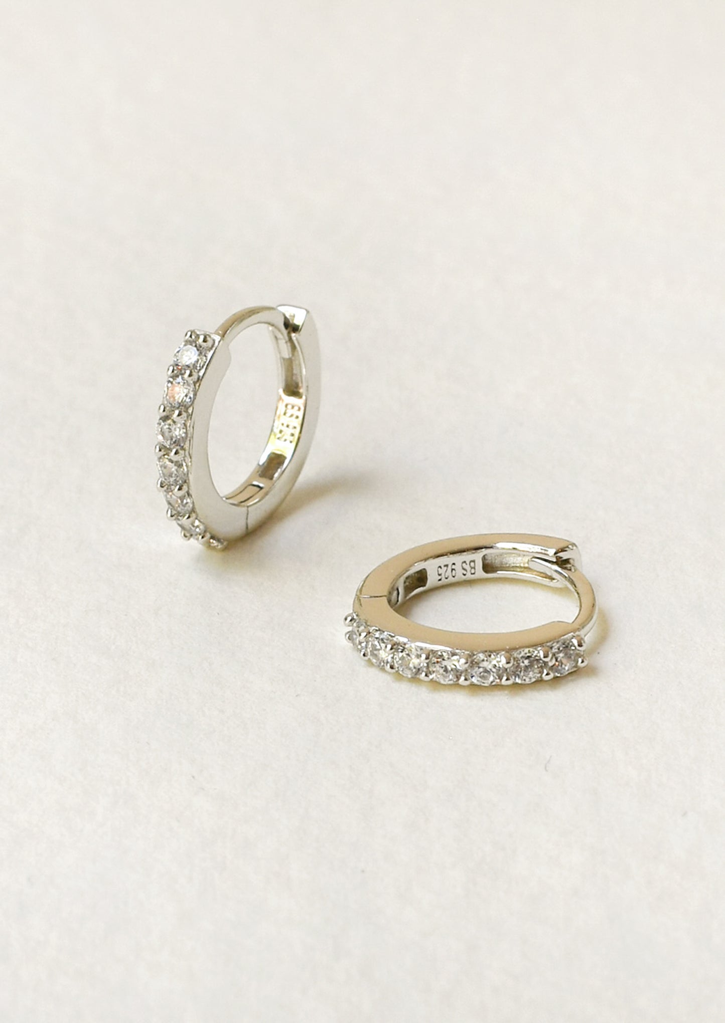 A pair of small huggie hoop earrings with clear pavé-set stones.