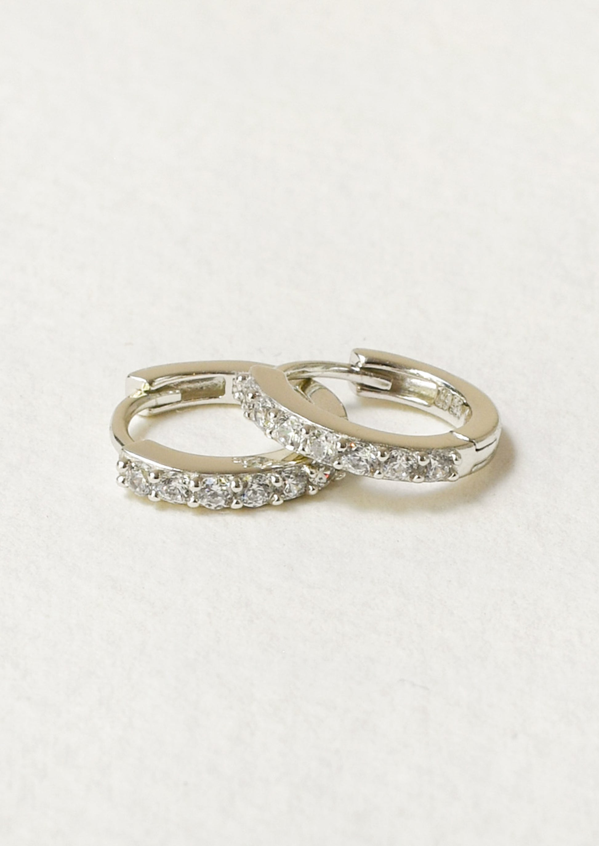 A pair of small huggie hoop earrings with clear pavé-set stones.