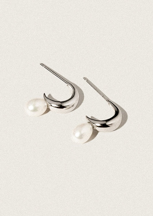 A pair of silver hoop earrings with attached pearl.