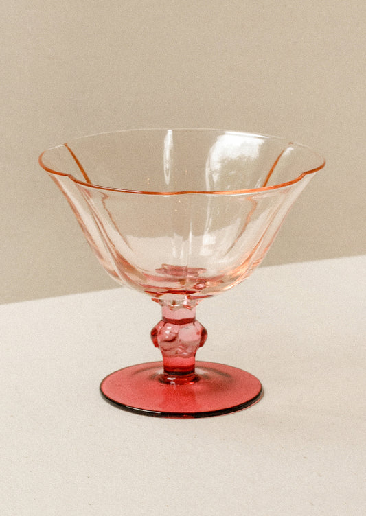 A short coupe glass with peach top and fuchsia stem.
