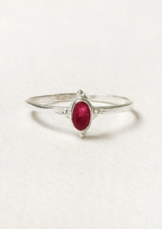 A sterling silver ring with a thin band and a small oval ruby stone in the center.