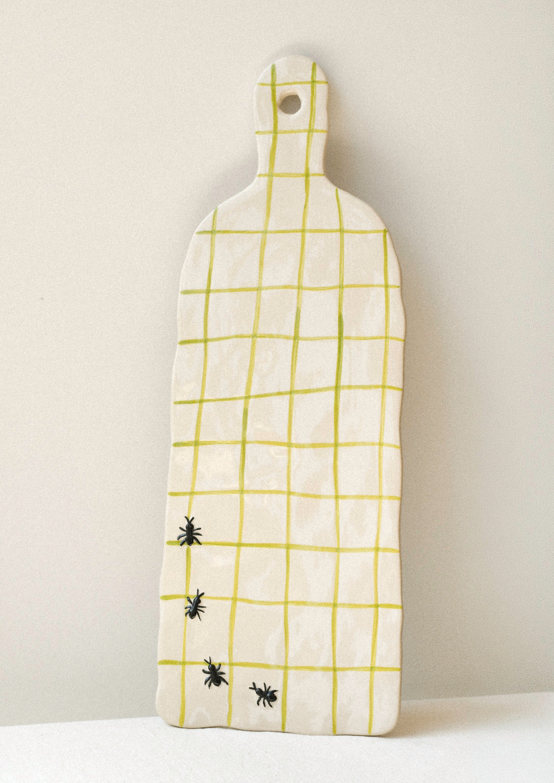 A large ceramic serving platter with green grid stripes and illustrated black ants in the corner.