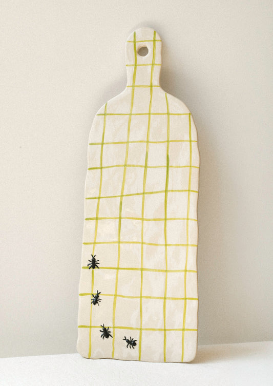 A large ceramic serving platter with green grid stripes and illustrated black ants in the corner.