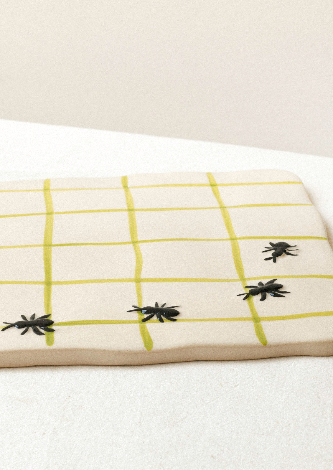 A large ceramic serving platter with green grid stripes and illustrated black ants in the corner.