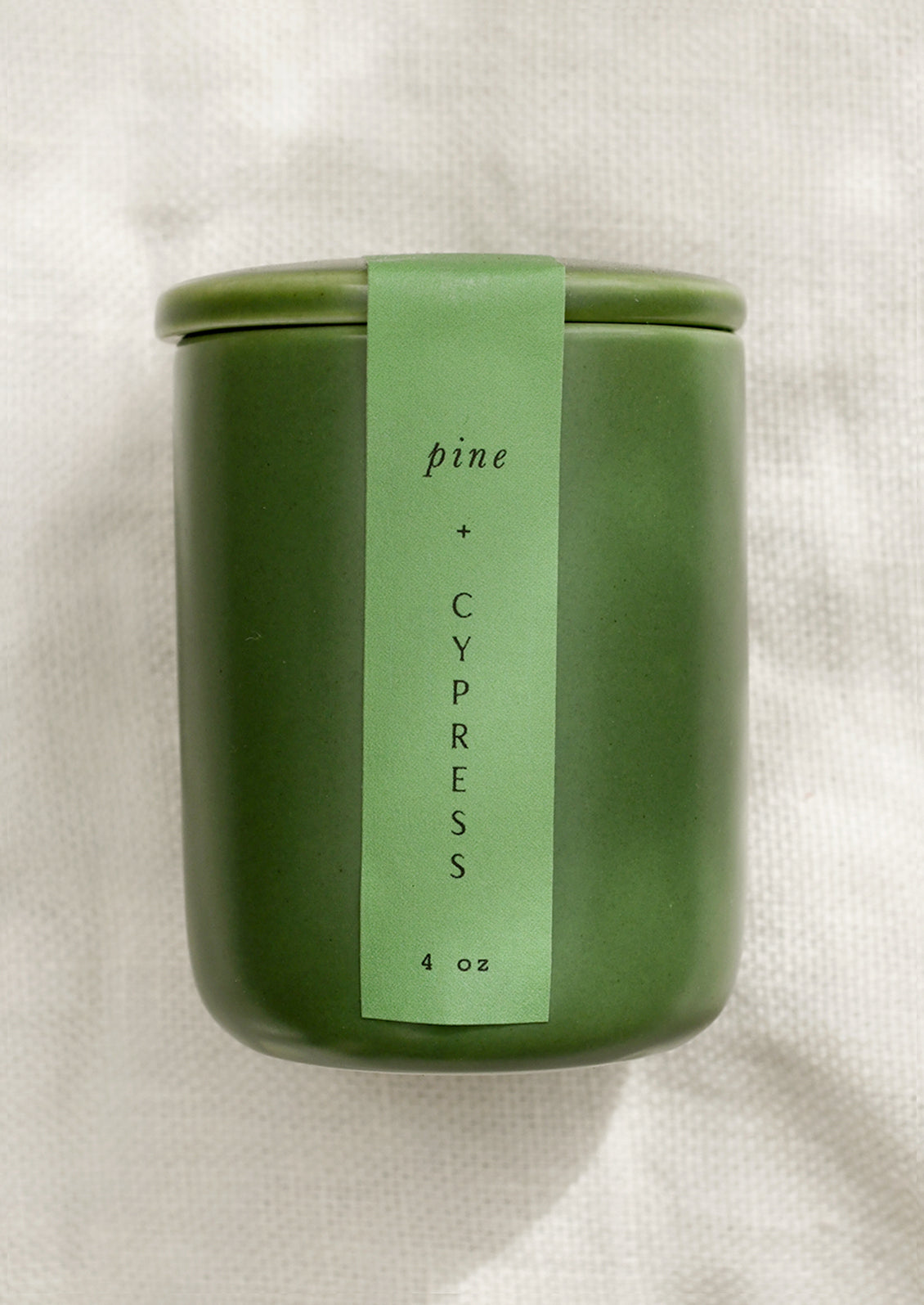 A small candle in lidded green ceramic jar in Pine and Cypress scent.