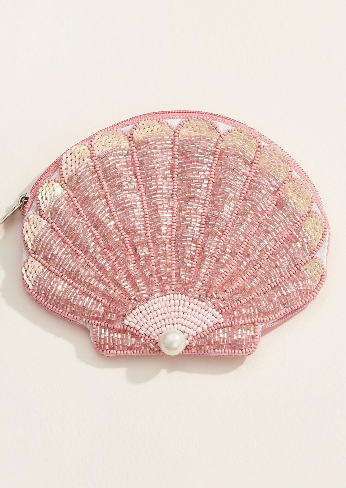 Pink shell-shaped pouch with beading and a pearl on a light beige background