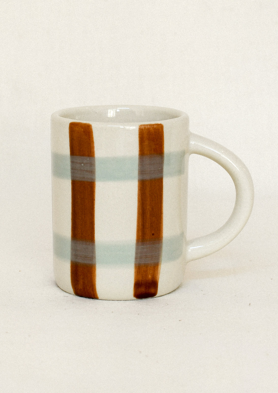 A white ceramic mug with a handle, decorated with two vertical brown stripes and two horizontal light blue-gray stripes, set against a plain off-white background.