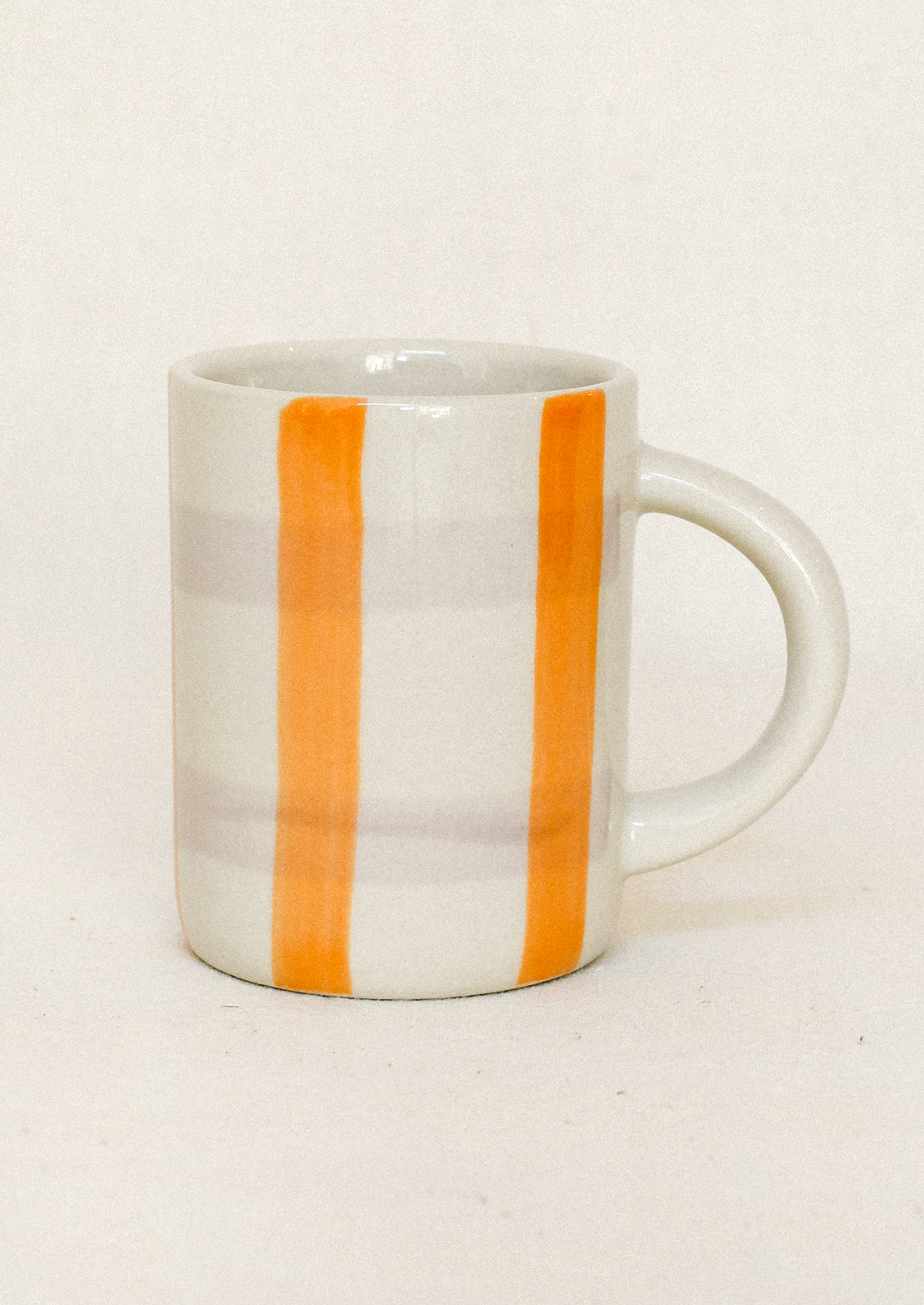 A white ceramic mug with two vertical orange stripes and faint horizontal gray stripes, shown against a plain off-white background.