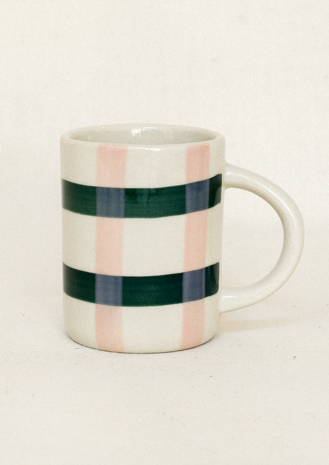 A white ceramic mug with a handle, decorated with hand-painted vertical stripes in dark green, dusty pink, and navy blue, set against a plain off-white background.