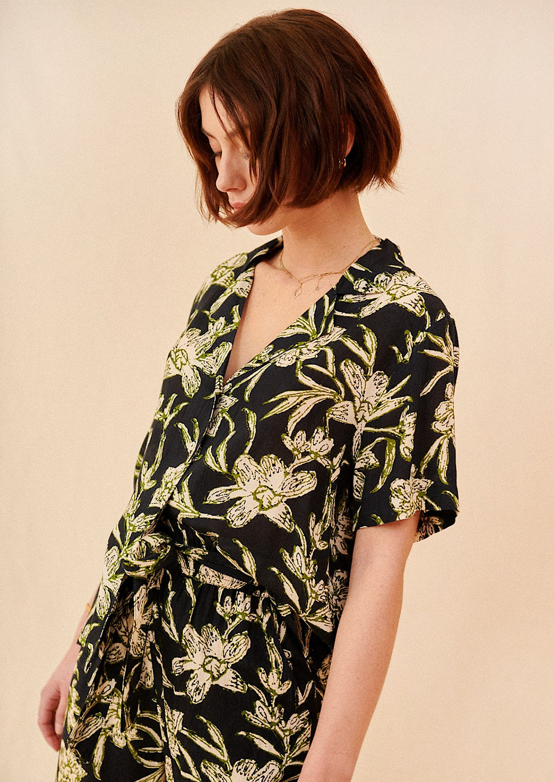 A woman wearing a v-neck collared shirt in black with green and cream floral print.