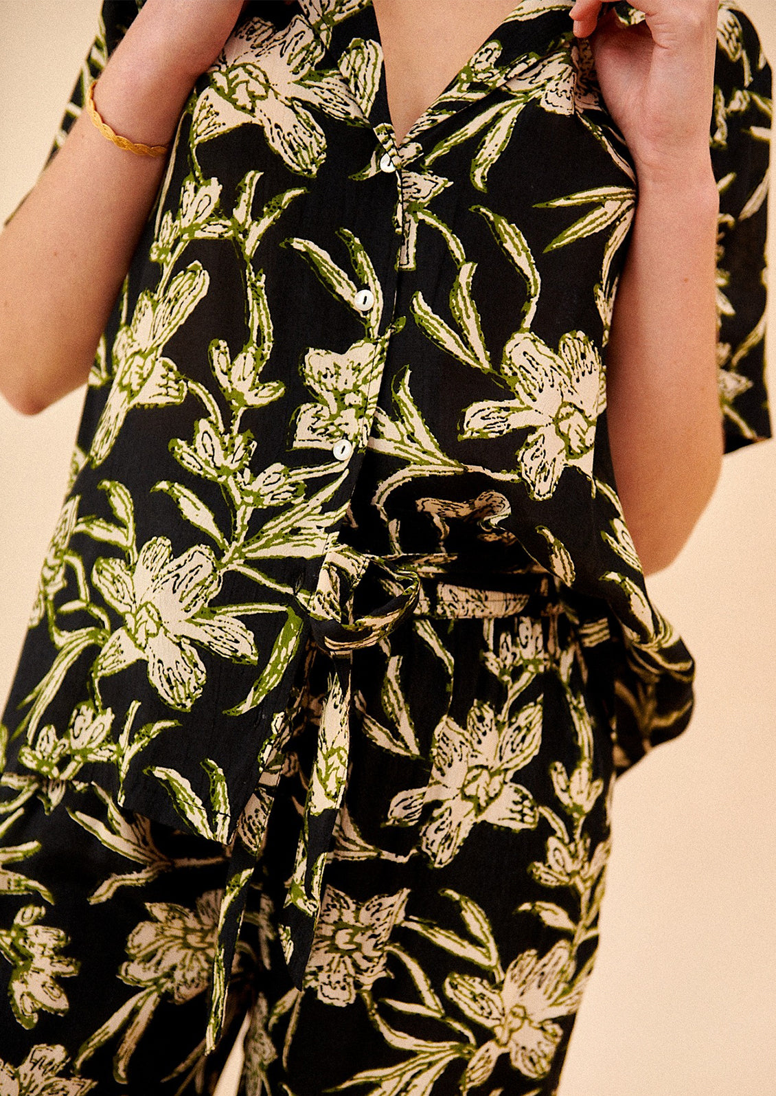 A woman wearing a v-neck collared shirt in black with green and cream floral print.
