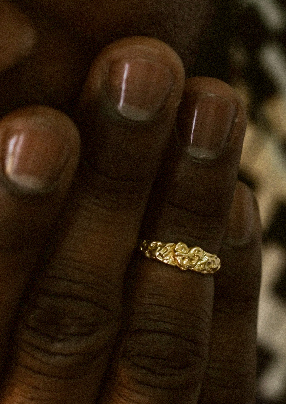 A small brass pinky ring with intricate detailing on a hand.