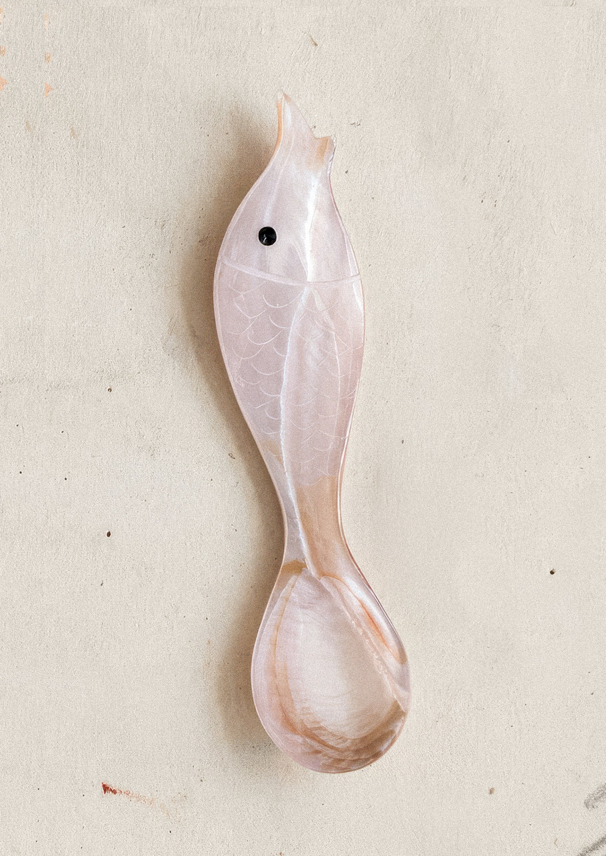 Decorative fish-shaped spoon in pink on a light gray background