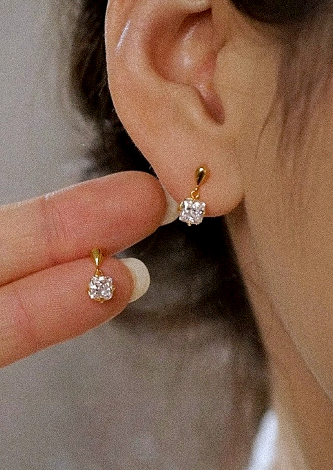 A woman wearing a pair of gold earrings with a princess cut cubic zirconia.