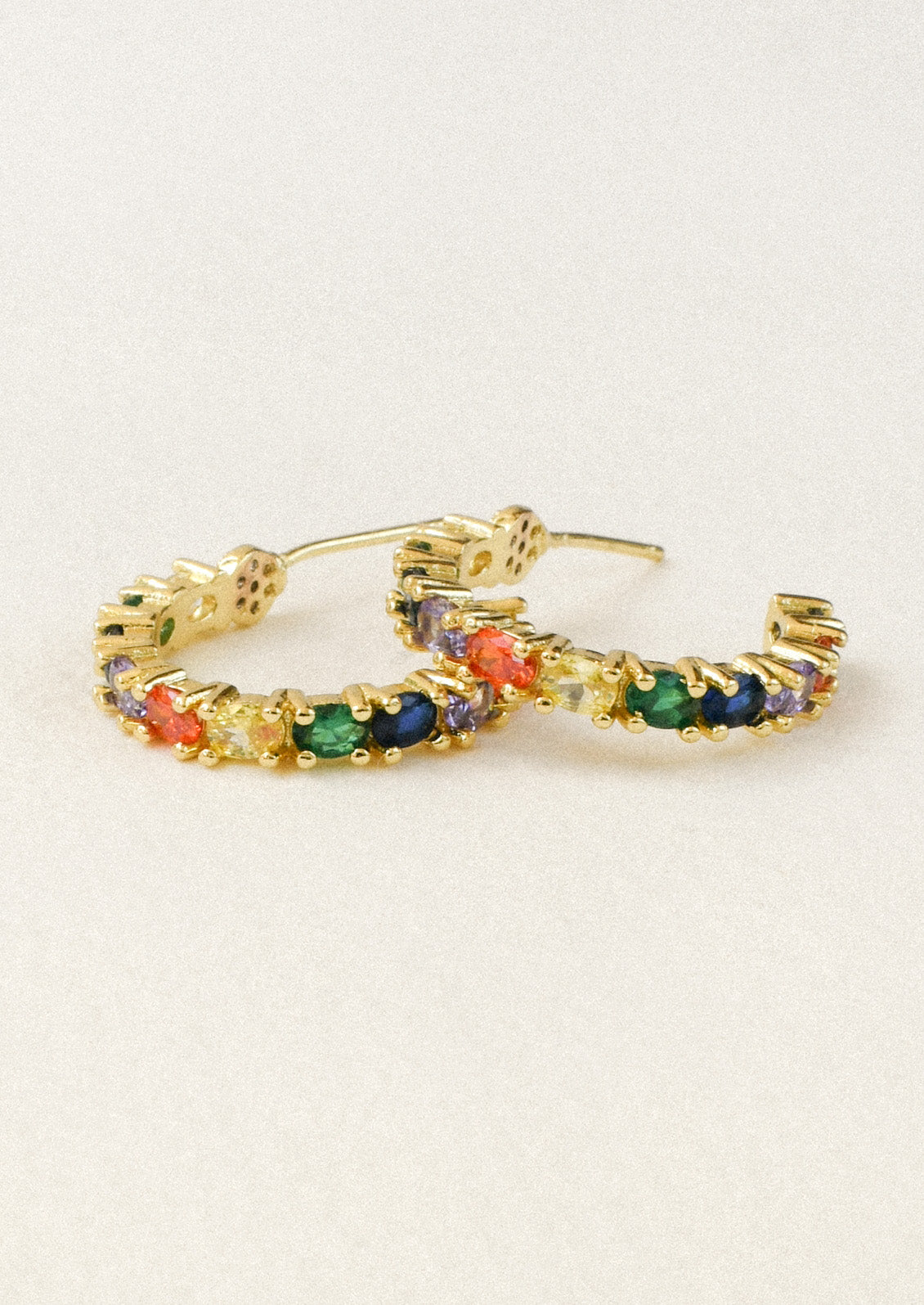A pair of gold hoop earrings adorned with various colored gems sitting on a white background.