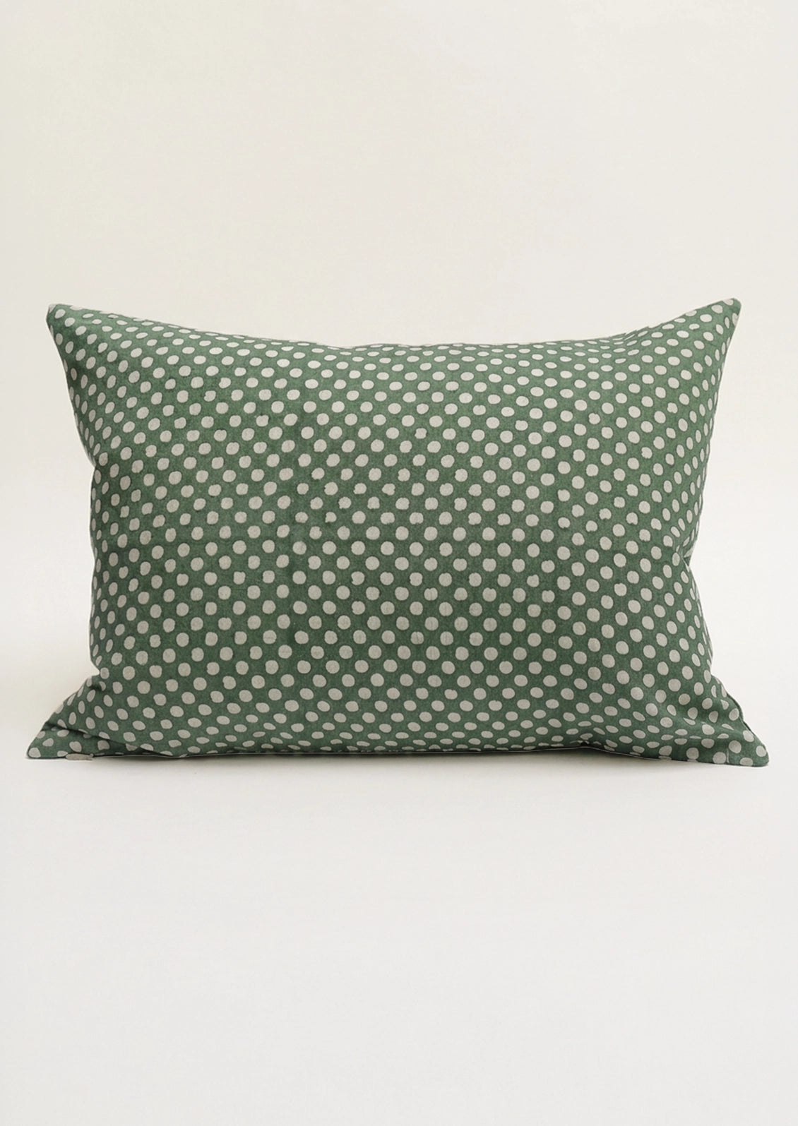 A lumbar throw pillow in green with white polka dots.