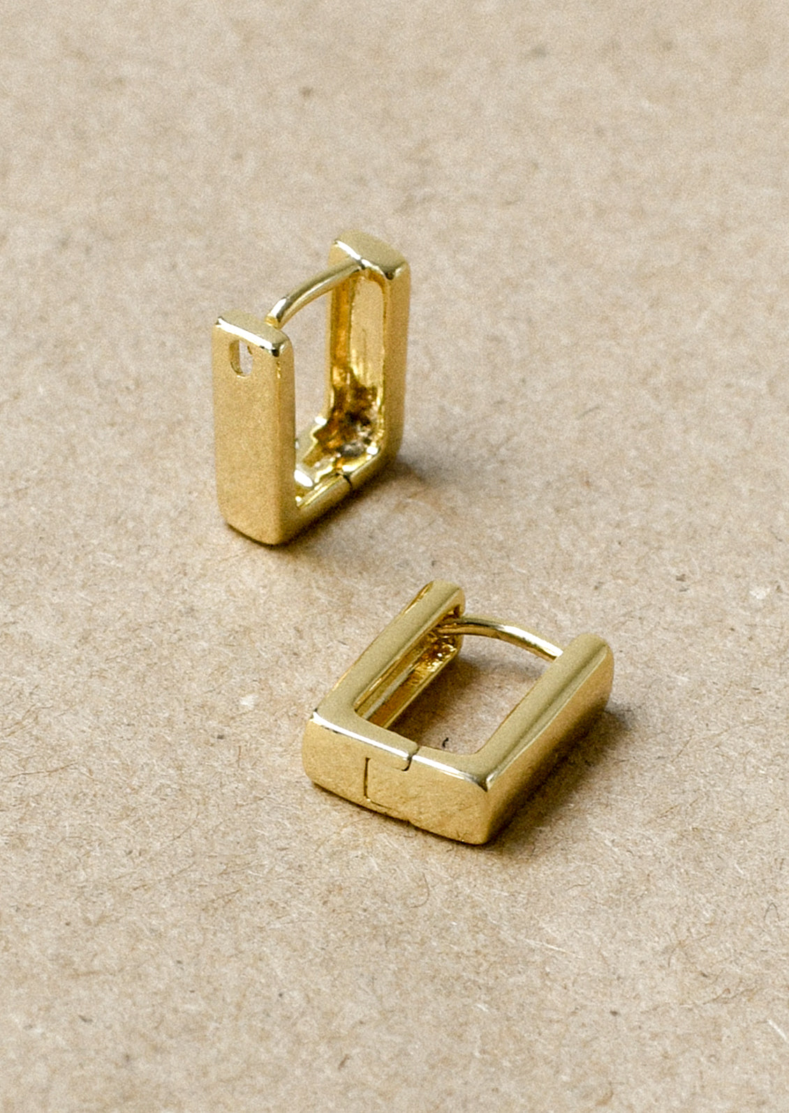 A pair of gold rectangular huggie earrings.